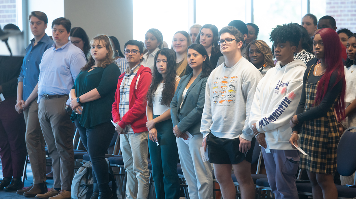 A group of young men and women stand at the front of a conference room.